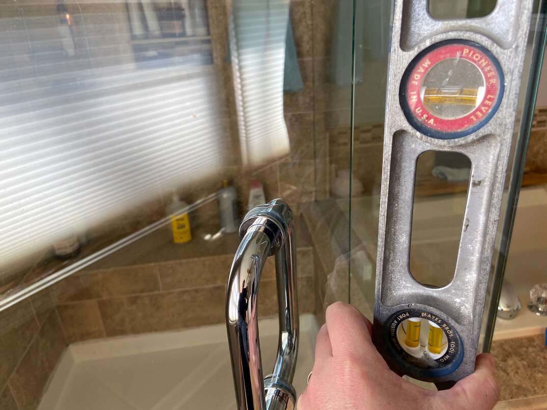 handyman installing glass shower doors using a level