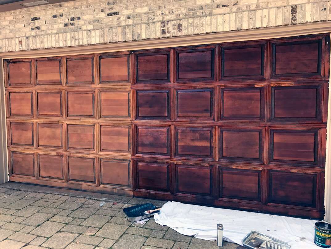 Unfinished red oak garage door with stain being applied.