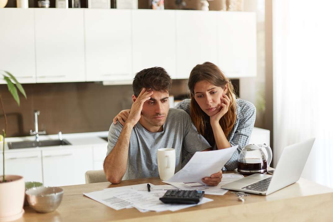 Unhappy American couple managing home accounts in kitchen, trying to save some money by cutting family expenses. Finances, bankruptcy, taxes, money, accounting and financial problems concept