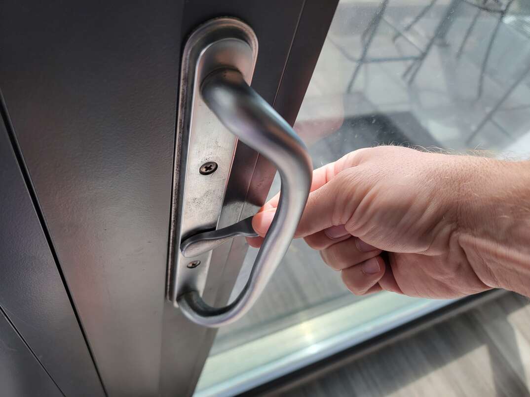 human hand flipping the switch to lock a sliding glass door from the inside, human hand, hand, human, flipping switch, switch, lock, locking door, locking sliding glass door, sliding glass door, door, glass, window, natural light, gray metal, metal, gray