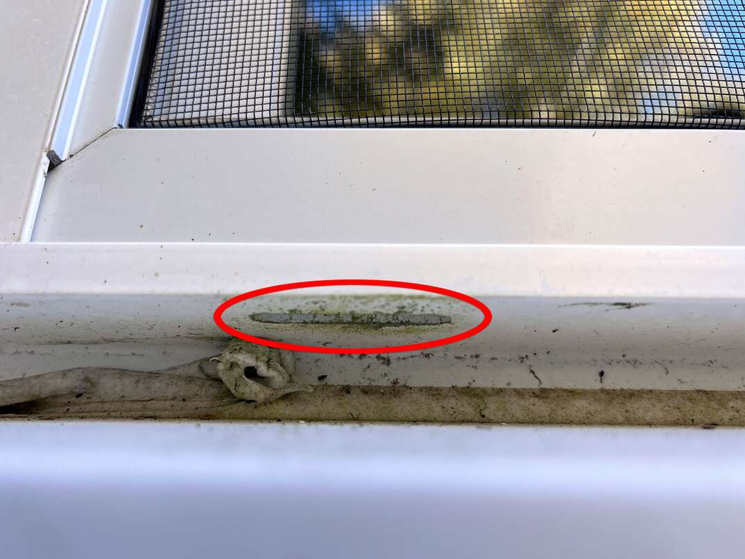 Close up shot taken from underneath a vinyl window showing the weep hole where water drains out.