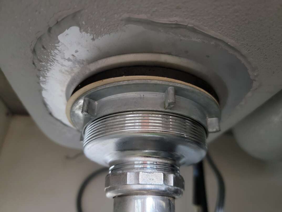 Underside view of kitchen sink shows where the cylindrical sink flange connects to the sink basin.