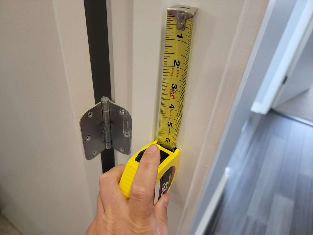 Person using yellow tape measure to measure 6 inches on a white door frame.