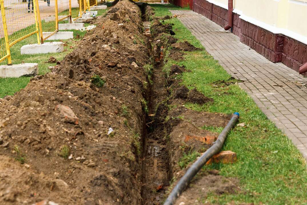 A long and deep trench dug up in a yard to lay in a drainage pipe for a trench drain