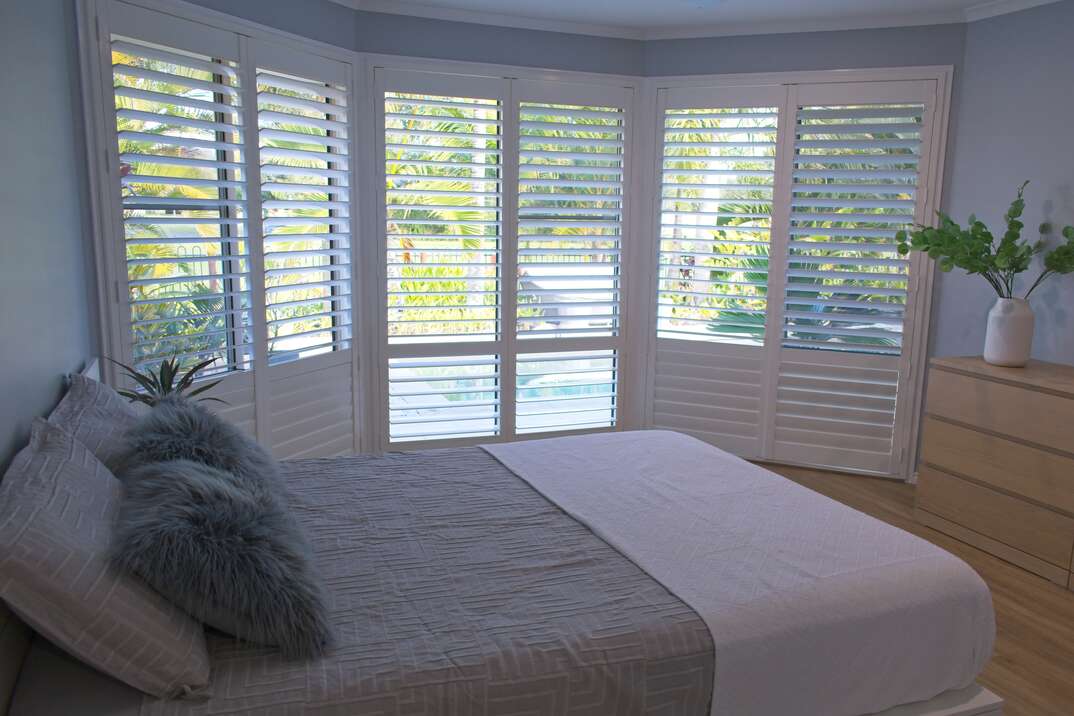 white wood Plantation shutters adorn the windows of a residential bedroom