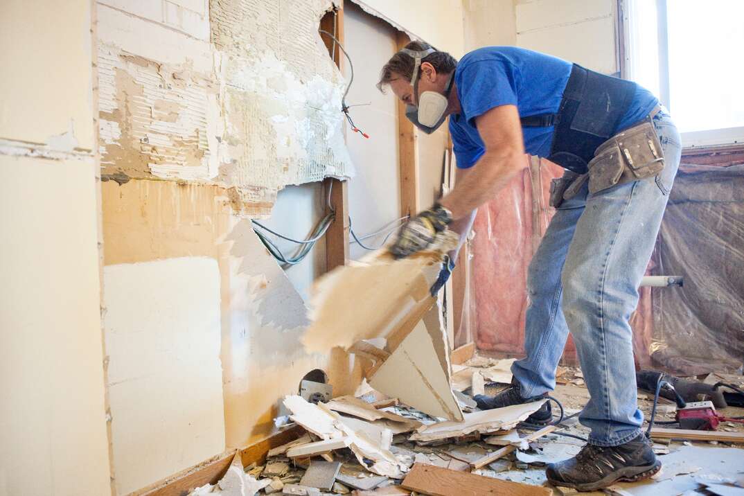 a contractor using PPE carefully demolished a wall in a residential home