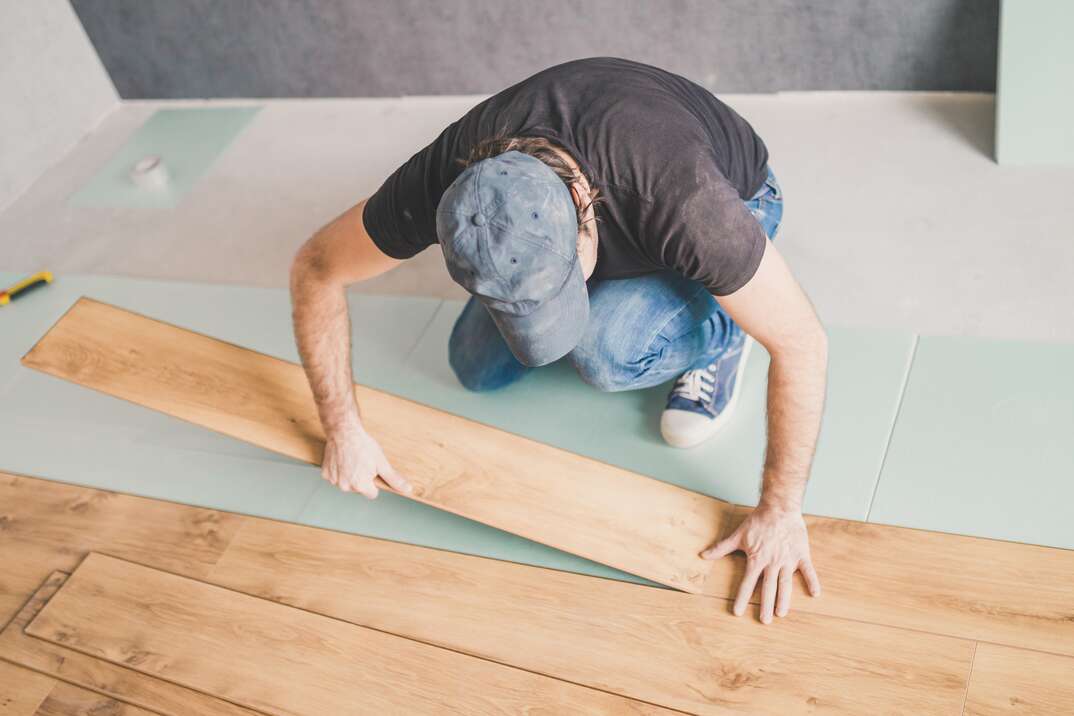 A flooring installation worker locks together a length of wood flooring as he installs planks on a half finished floor, wood floor, hardwood floor, floor, flooring wood planks, planks, wood, hardwood, worker, floor installer, male, man, worker, laminate flooring, laminate floor, click-together flooring, floating hardwood floor, floating