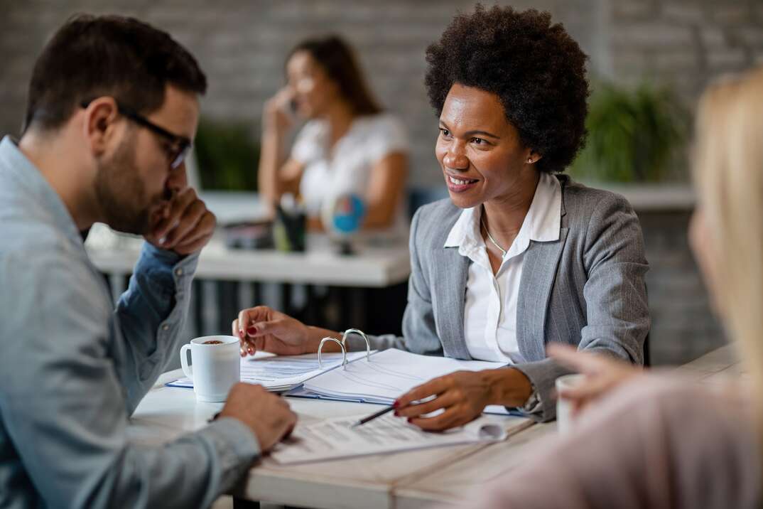 Black smiling insurance agent talking with a client while going through paperwork during the meeting in the office.