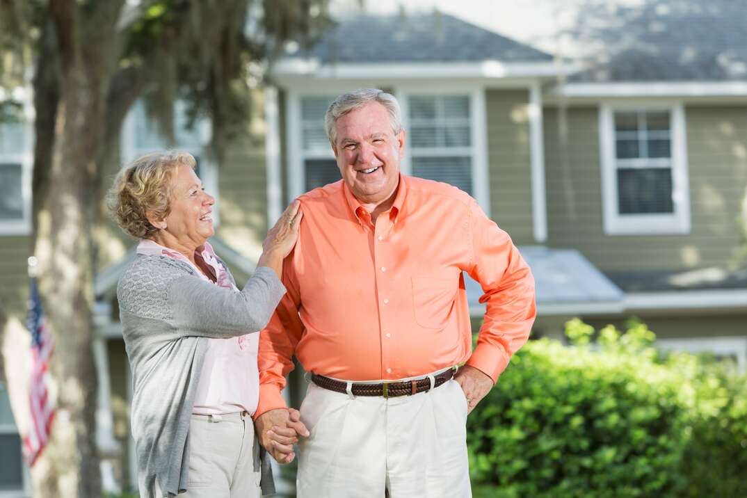 Senior couple standing in front of house.