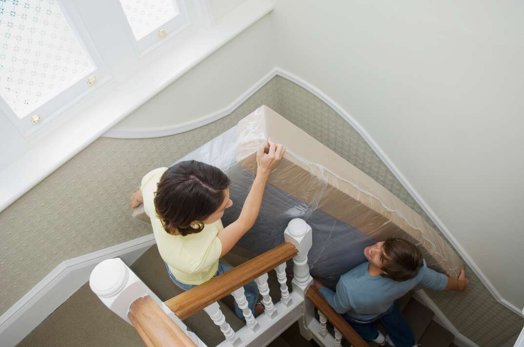 Couple carrying mattress upstairs