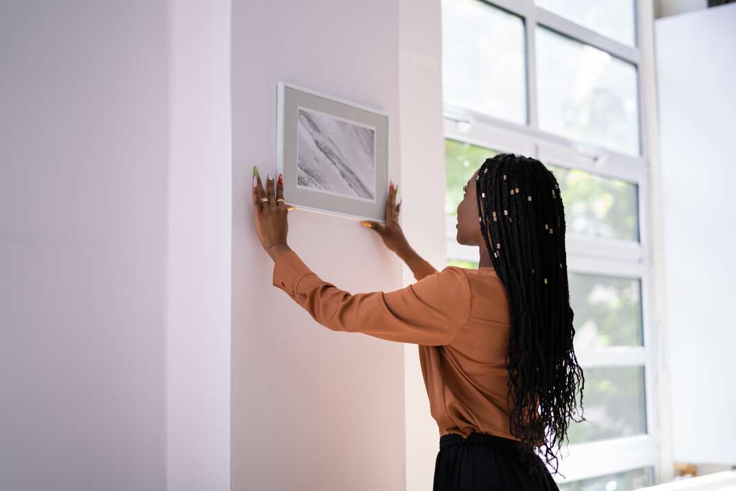 Young Woman Putting Photo Frame On White Wall
