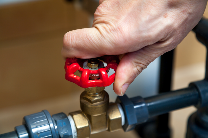 Hand turns the red round handle of a valve on a plastic pipe