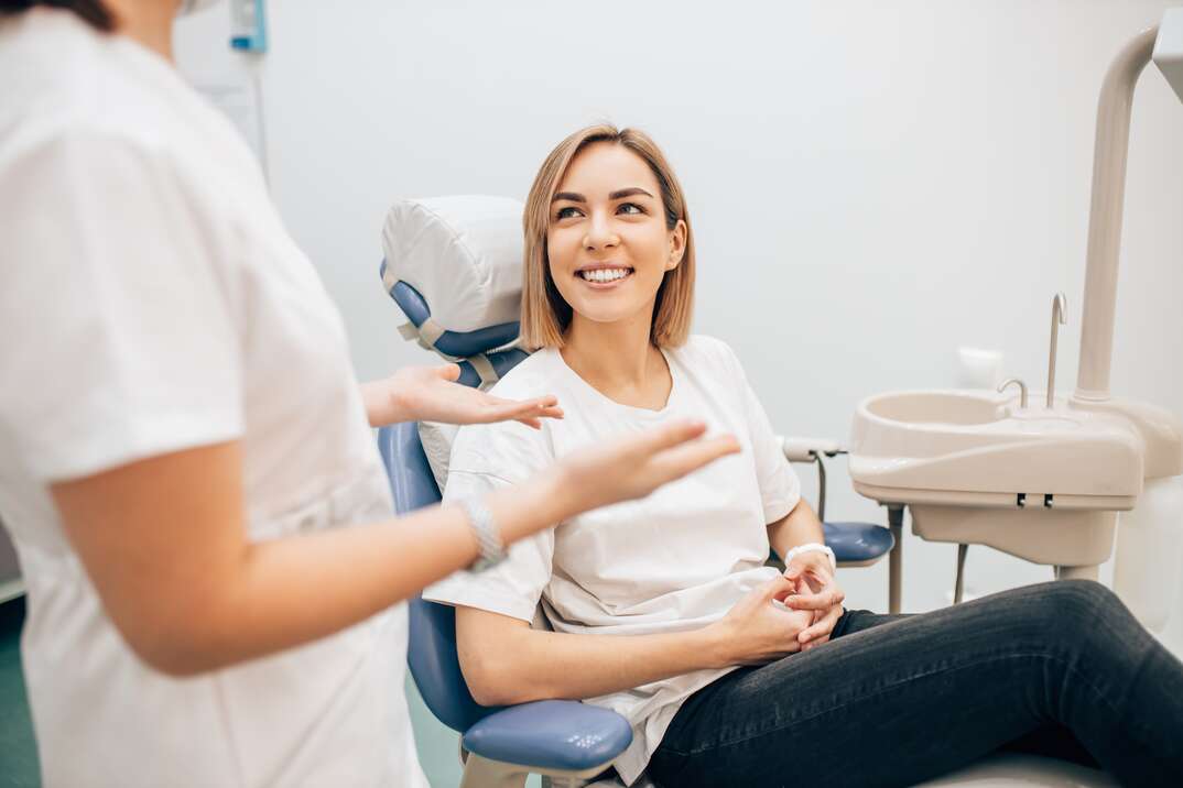 An ostensibly female dentist explains something to the dental patient who is seated in the dentist char smiling among your standard dentist office equipment, dentist, dental, dentist office, dental patient, smiling, teeth, tooth, smile, dental chair, female dentist, female patient, patient