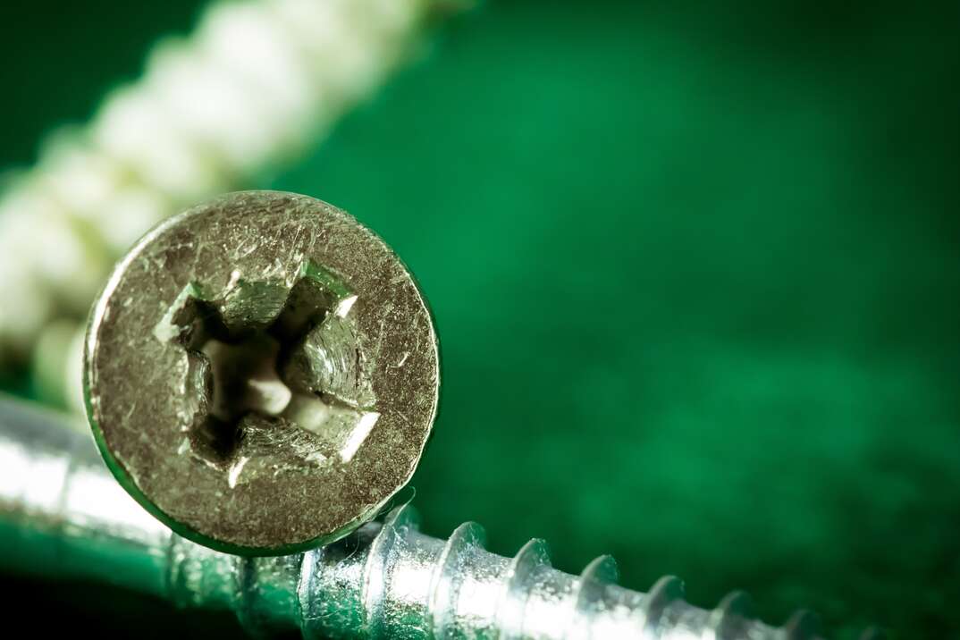The stripped out head of a screw is shown in extreme closeup with two other screws shown from the side against a green background, stripped screw, screw, stripped, damaged, damage, damaged screw, screws, green background, green, closeup photo, closeup, extreme closeup