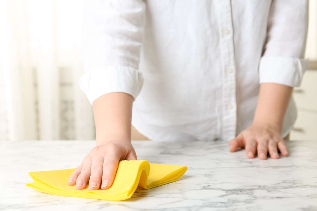 Woman wiping white marble table with rag indoors