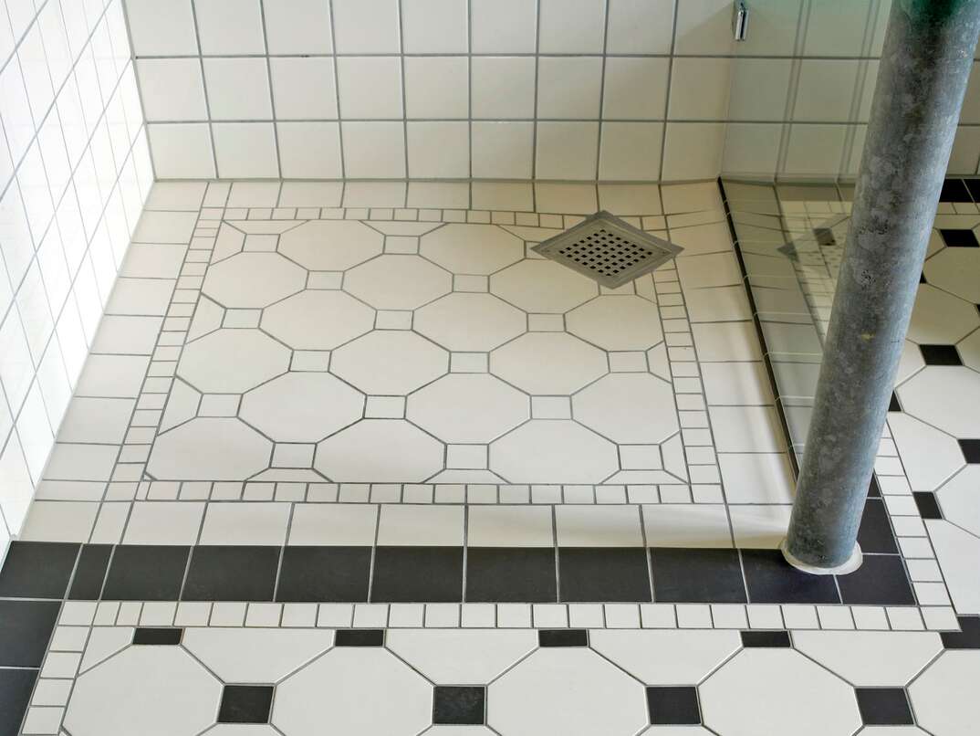 a large Wet room with black and white tiles and a stainless steel floor drain