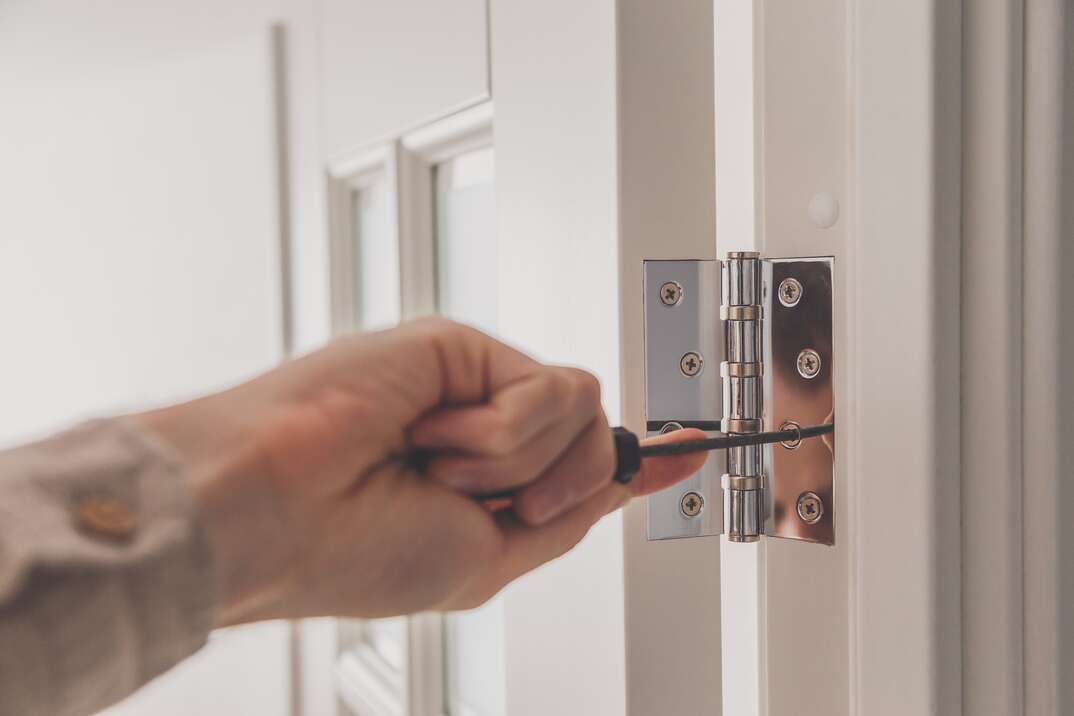 Man remove the door  Twists self-tapping screw with a screwdriver  Stainless door hinges on a white door