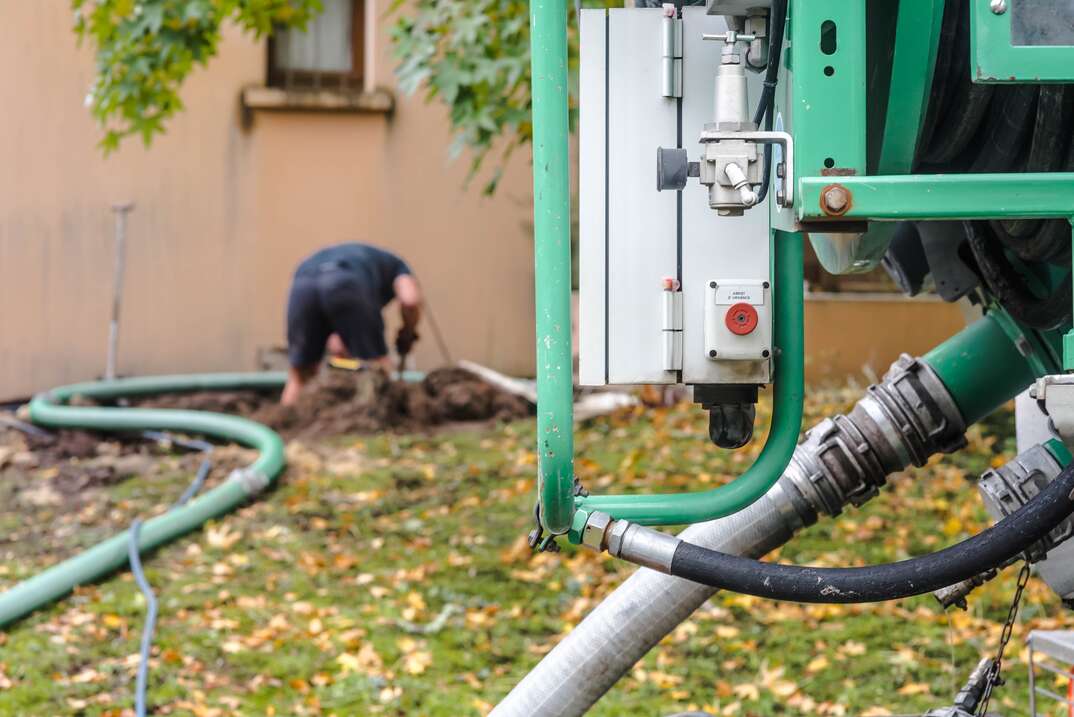 a man is pumping a septic tank from the backyard using a green hose from a large truck