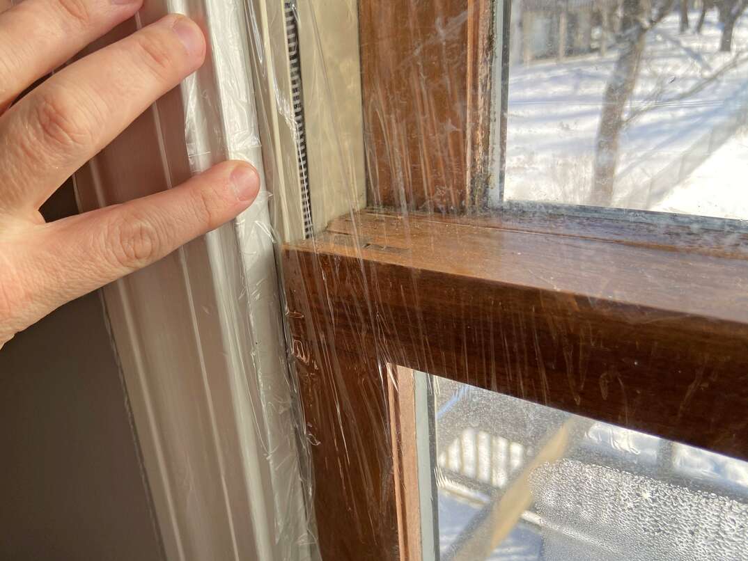 close up of window insulation film being applied with double-sided tape to the window frame