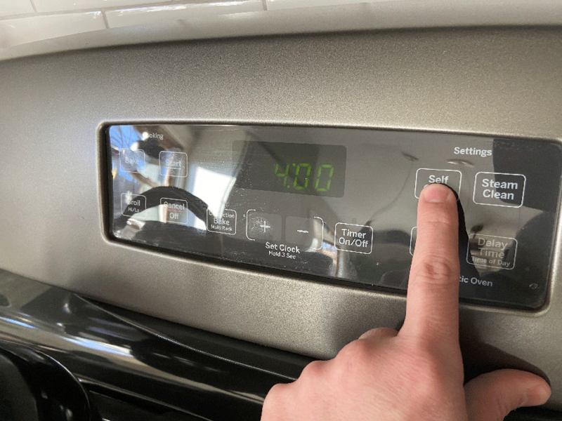 Person activating the self-cleaning feature on a GE oven