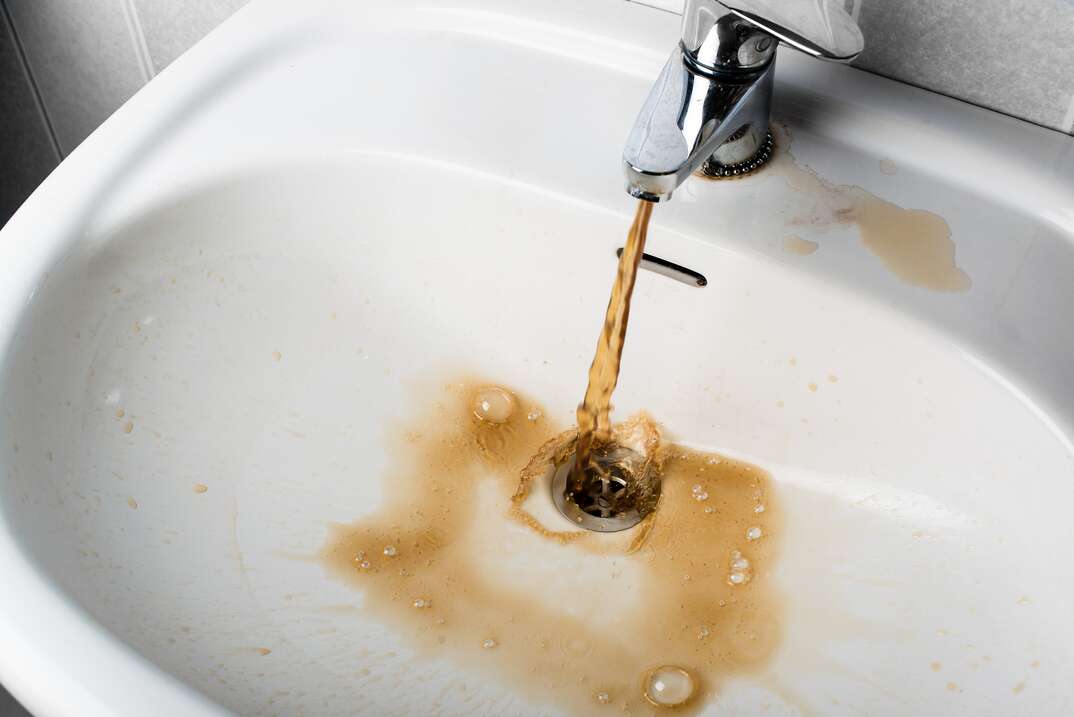 a residential sink with contaminated brown water flowing from it 