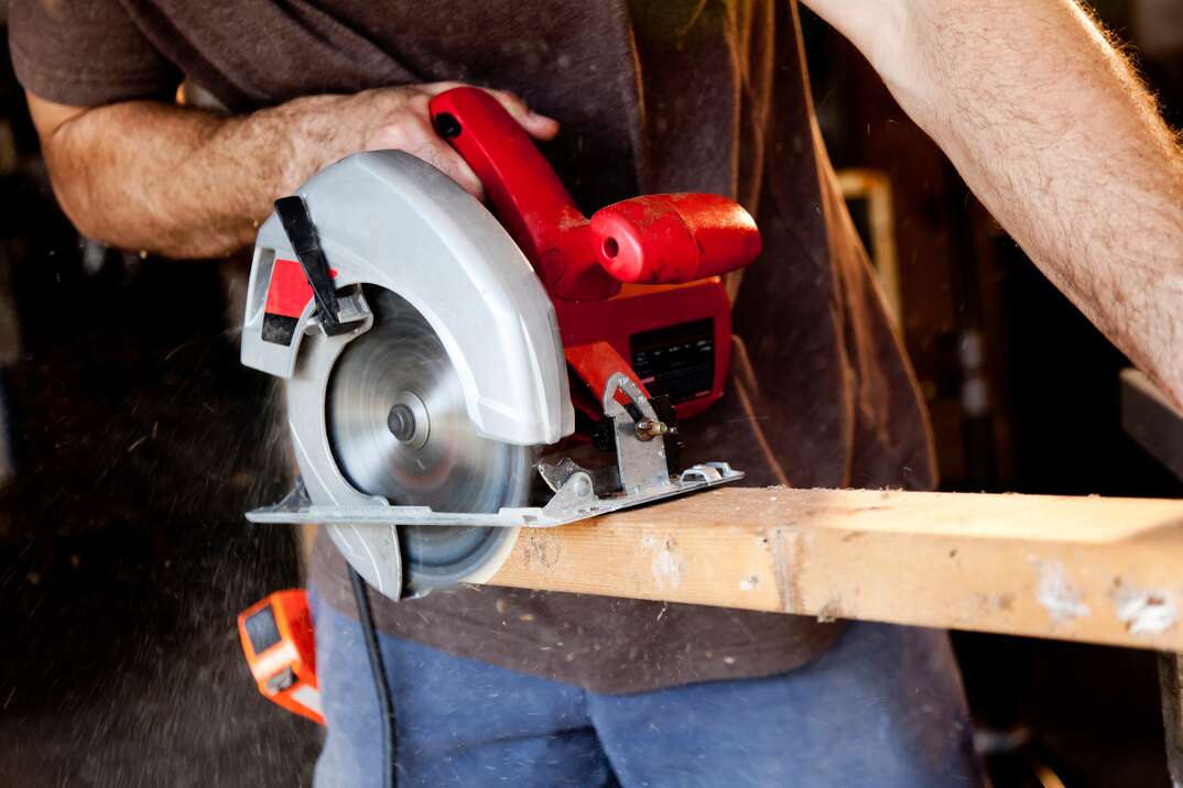 contractor uses a red circular saw to cut a 2x4 board