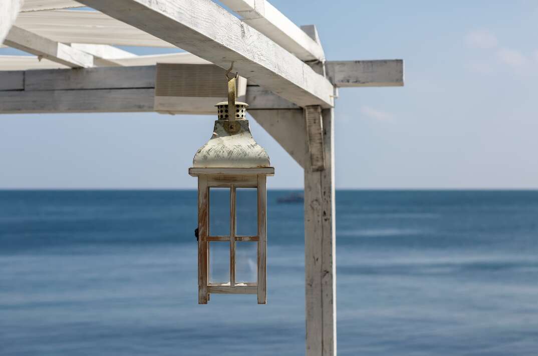 Painted Wooden lantern hangs from a bleached wood pergola overlooking the ocean