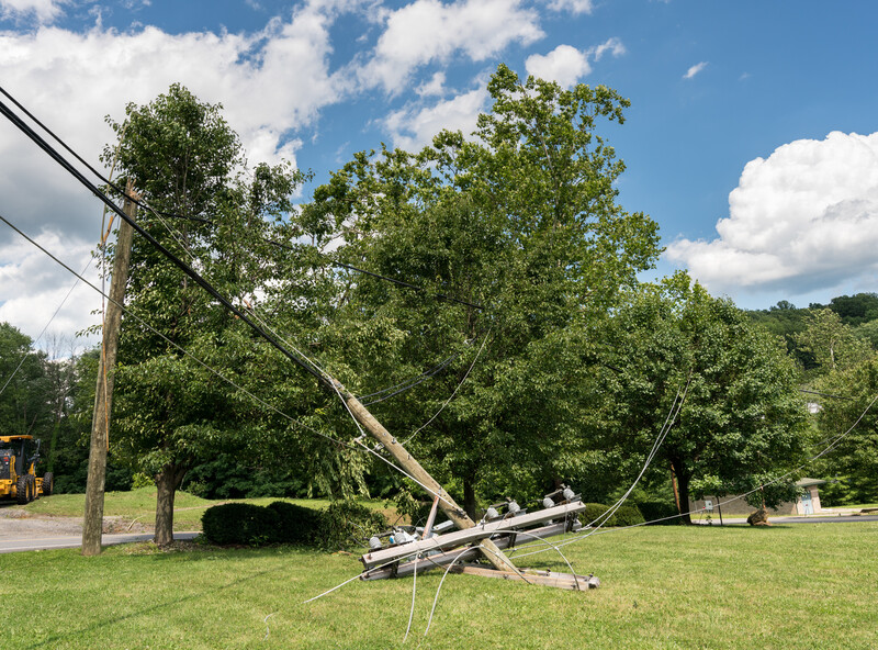 Broken snapped wooden power line post with electrical components on the ground after a storm