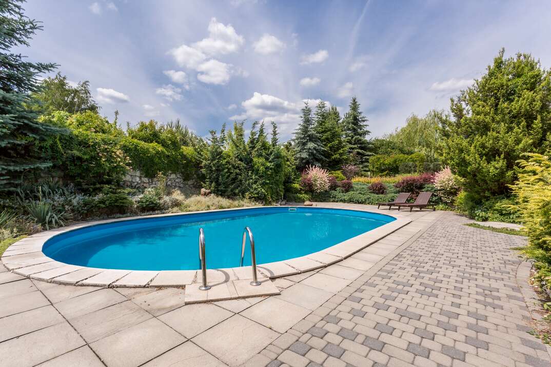 A backyard in-ground pool surrounded by brick pavers sparkles in the sun