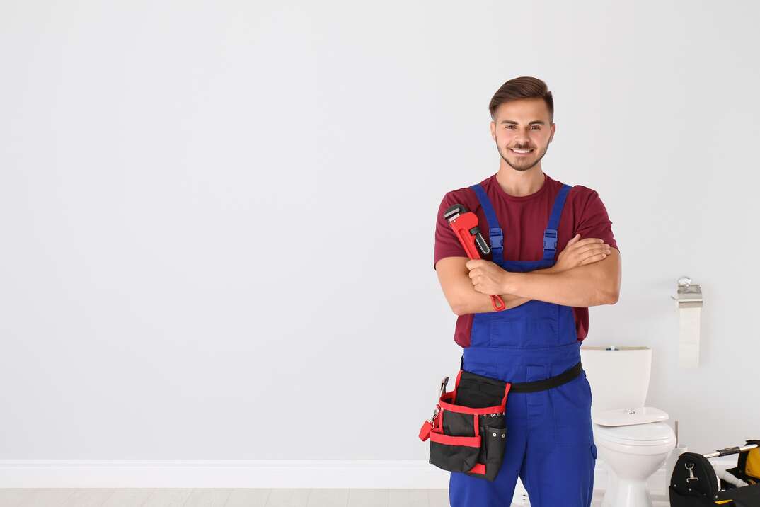 Young man with plumber wrench and toilet bowl on background