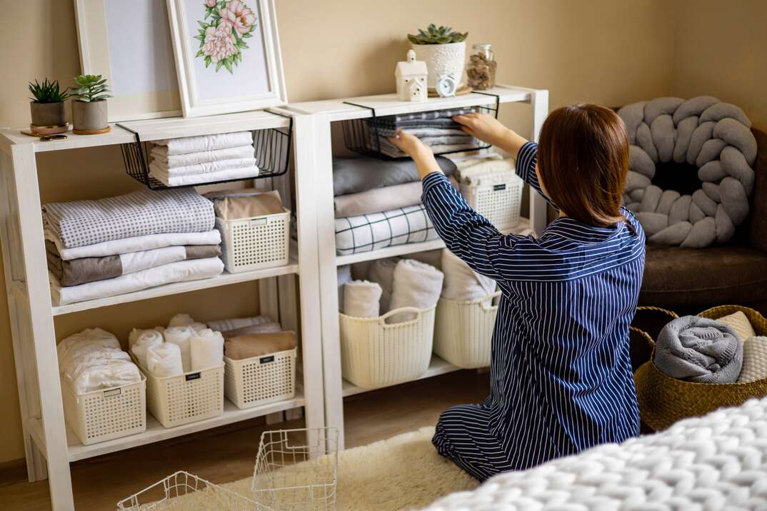 A woman with her back to the viewer crouches down next to well organized shelving as she puts something back in its place, shelving, shelves, well-organized, organized, organization, woman, bedroom