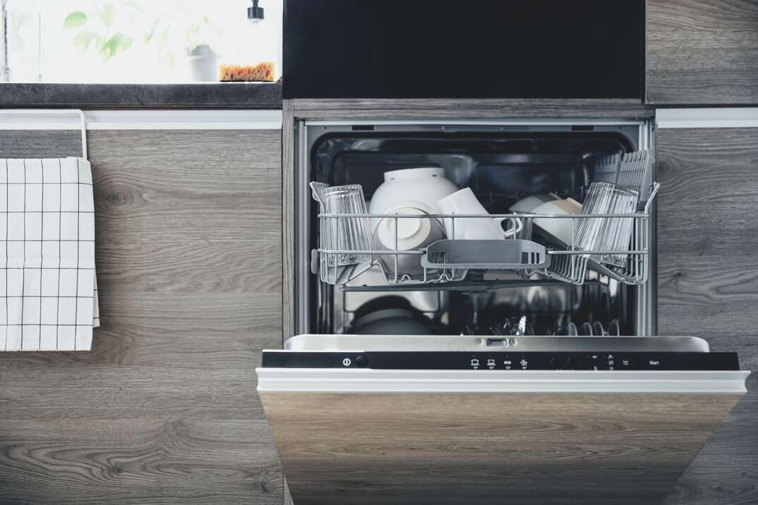 Front view of built-in opened dishwasher machine at kitchen with clean utensil