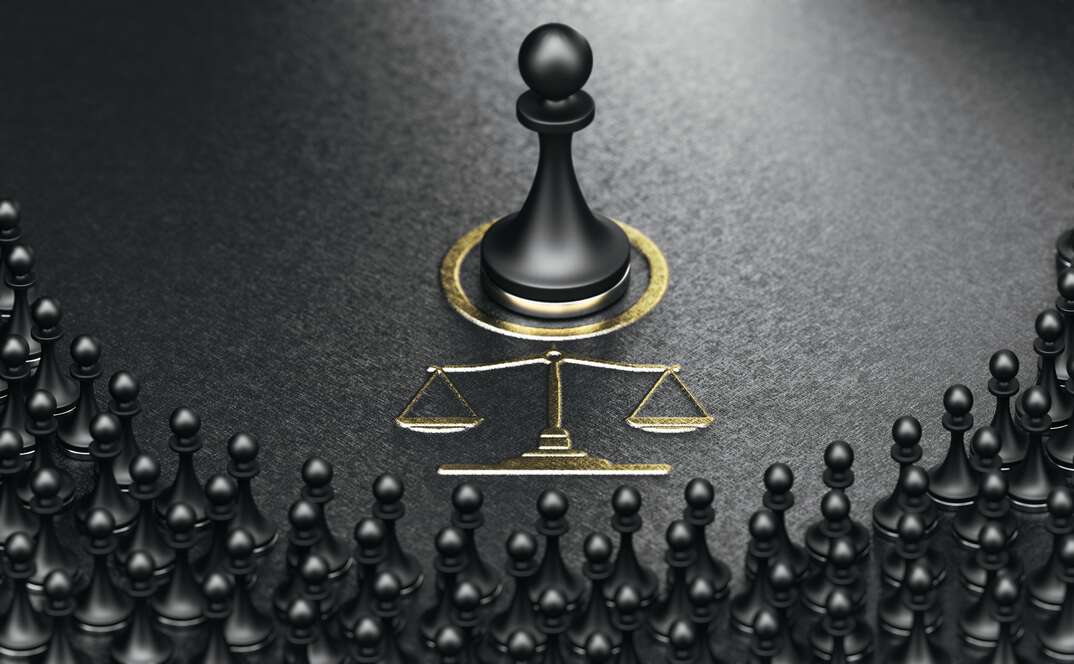 This photo illustration depicts a class action lawsuit using chessboard pawns as dozens of black colored pawns gathered in a semicircle facing a gold scale of justice and a single large black pawn sitting in the middle of a gold circle on a black floor, black colored, black background, pawns, chessboard pawns, pawn, chessboard, chess, scales of justice, scales, photo illustration, class action lawsuit, lawsuit, legal, civil suit, civil action