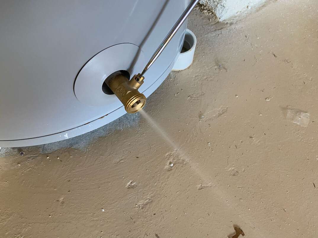 A homeowner uses a screwdriver to open the drain valve on a residential water heater 
