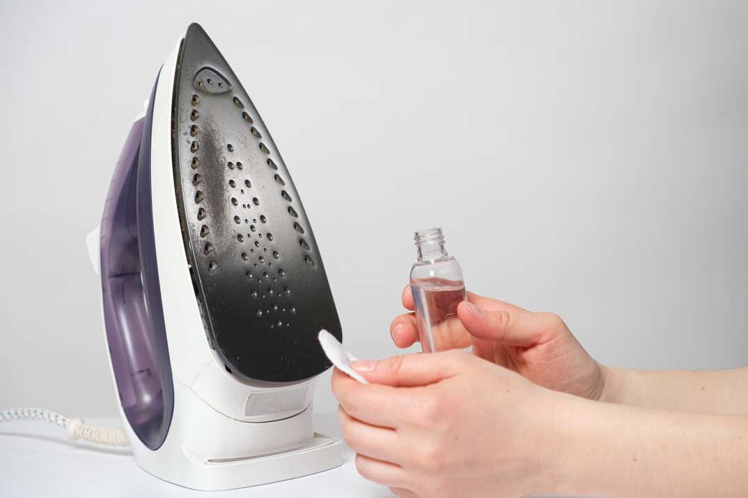 A woman cleans the sole of the iron from soot and scale with a special solution in a bottle and a cotton pad