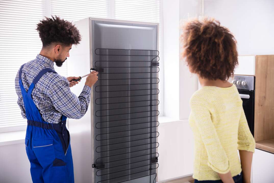 woman looking at technician repairing refrigerator with screwdriver in kitchen