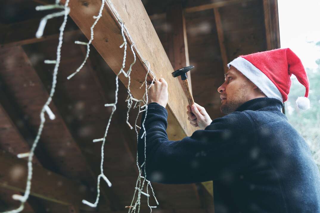 man with santa hat decorating house outdoor carport with christmas string lights