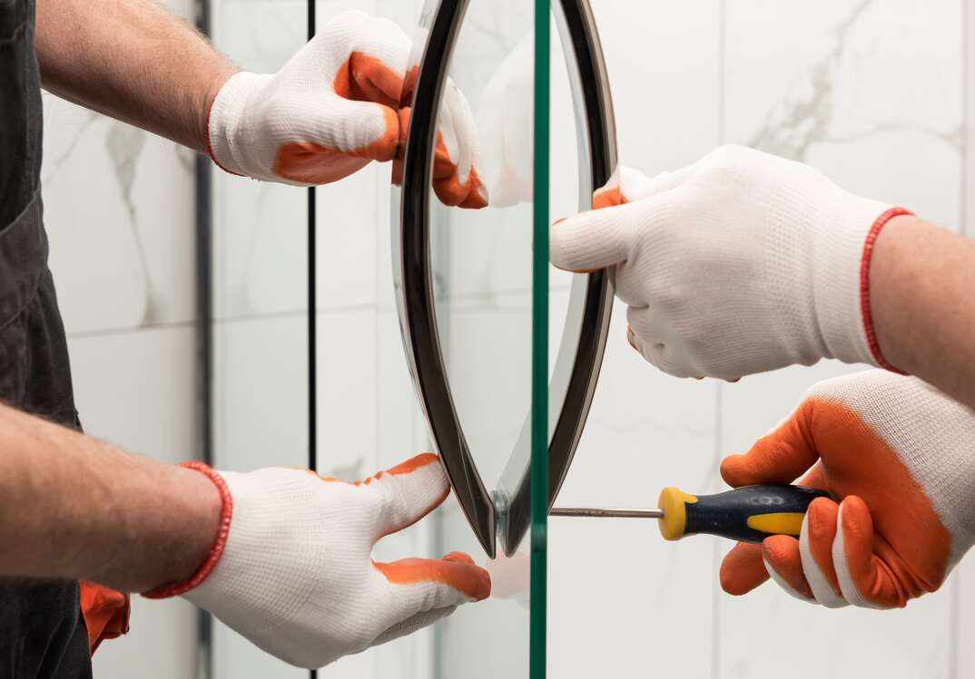 Workers are mounting door handles of the shower enclosure 