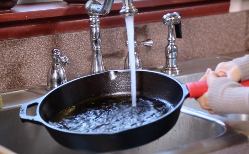 rinsing a cast iron pan in kitchen sink