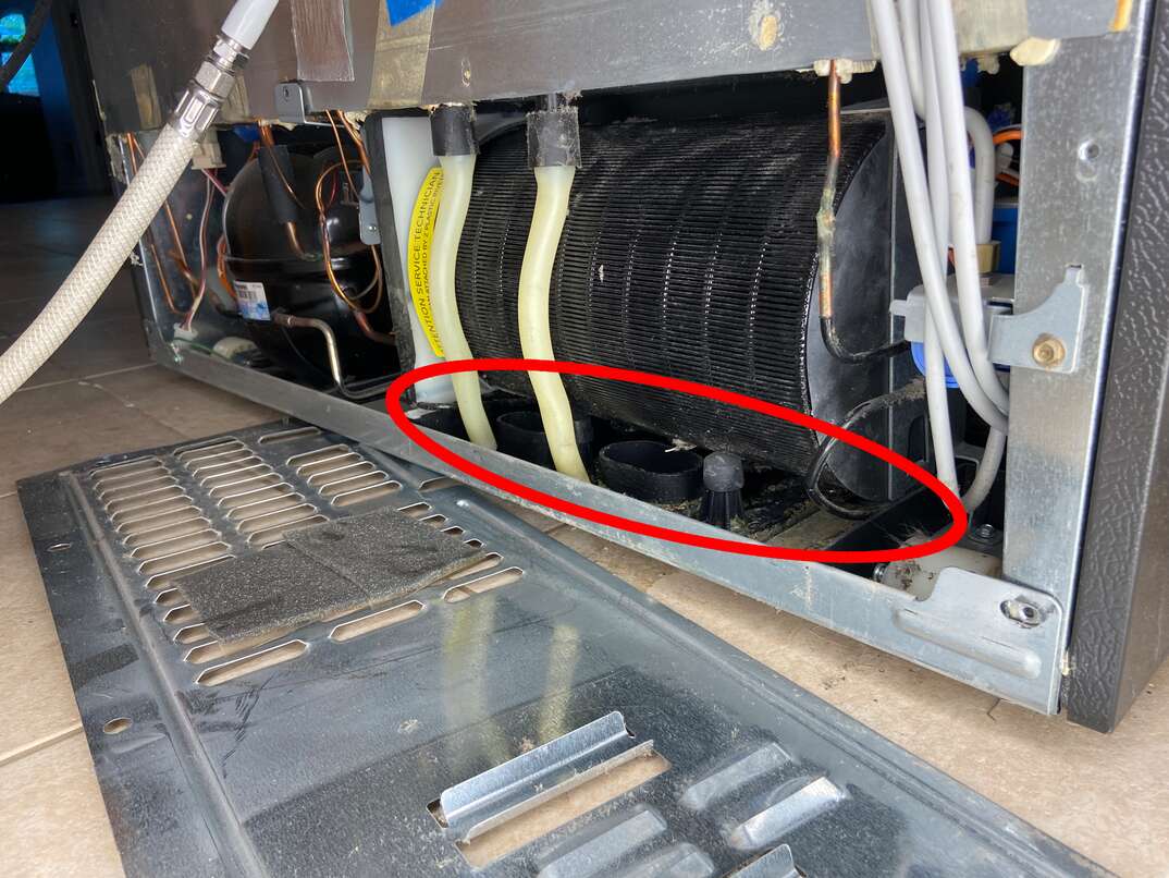 the back of a newer GE refrigerator shows the condenser cover removed and the condensate drip pan is underneath the coils circled in red.