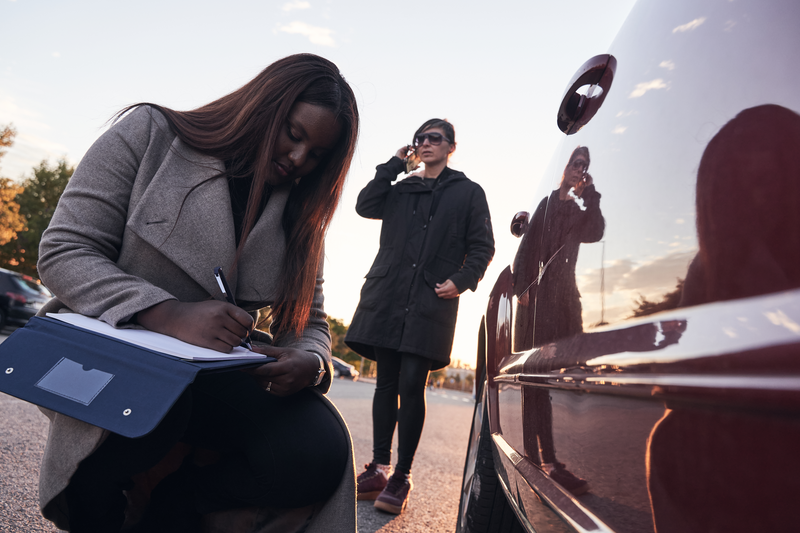 insurance agent examines the car while the driver talks on the mobile phone. Accident claim process. African-American woman checking the damage to the car after an accident. Concept of transportation.