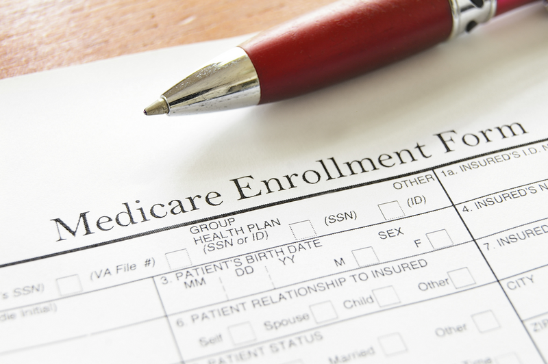 A Medicare enrollment form sits atop a tabletop with a red pen sitting on top of it, Medicare, medical coverage, medical form, form, document, medical, medicine, pen, ink pen, enrollment form, Medicare enrollment form