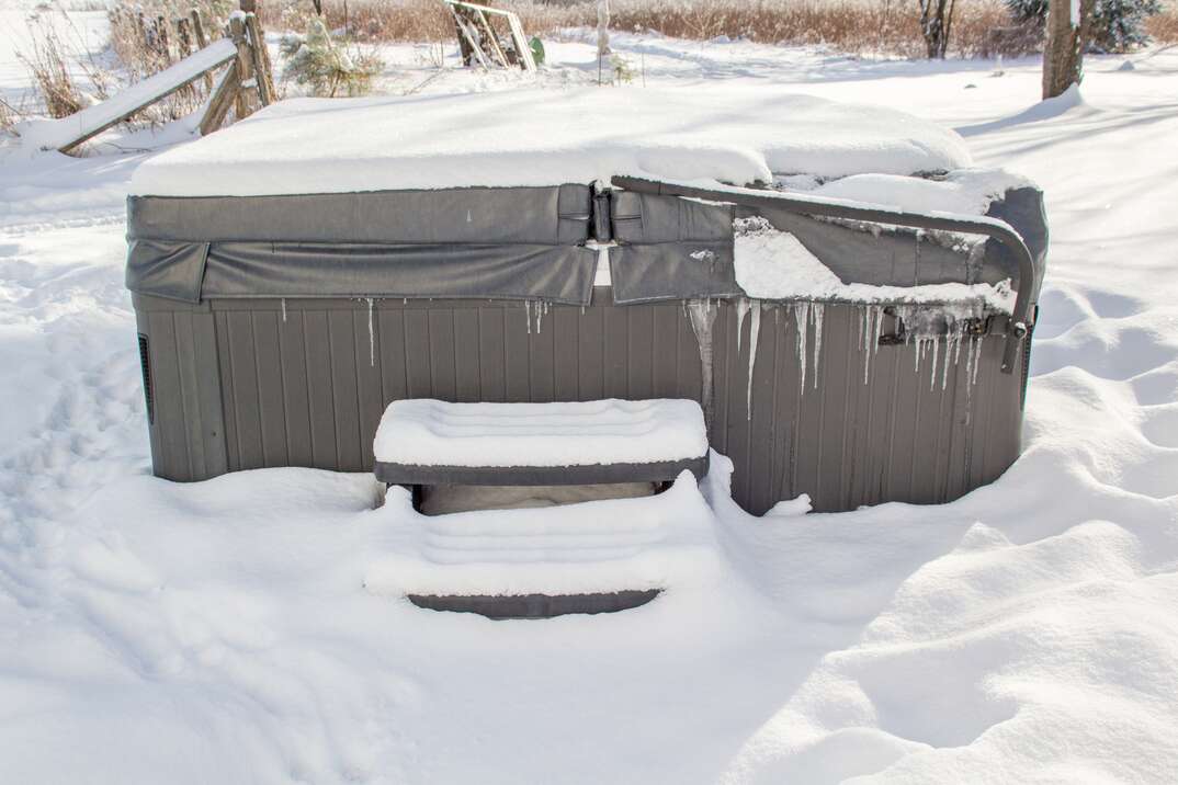 An outdoor hot tub is covered in snow and icicles in the winter