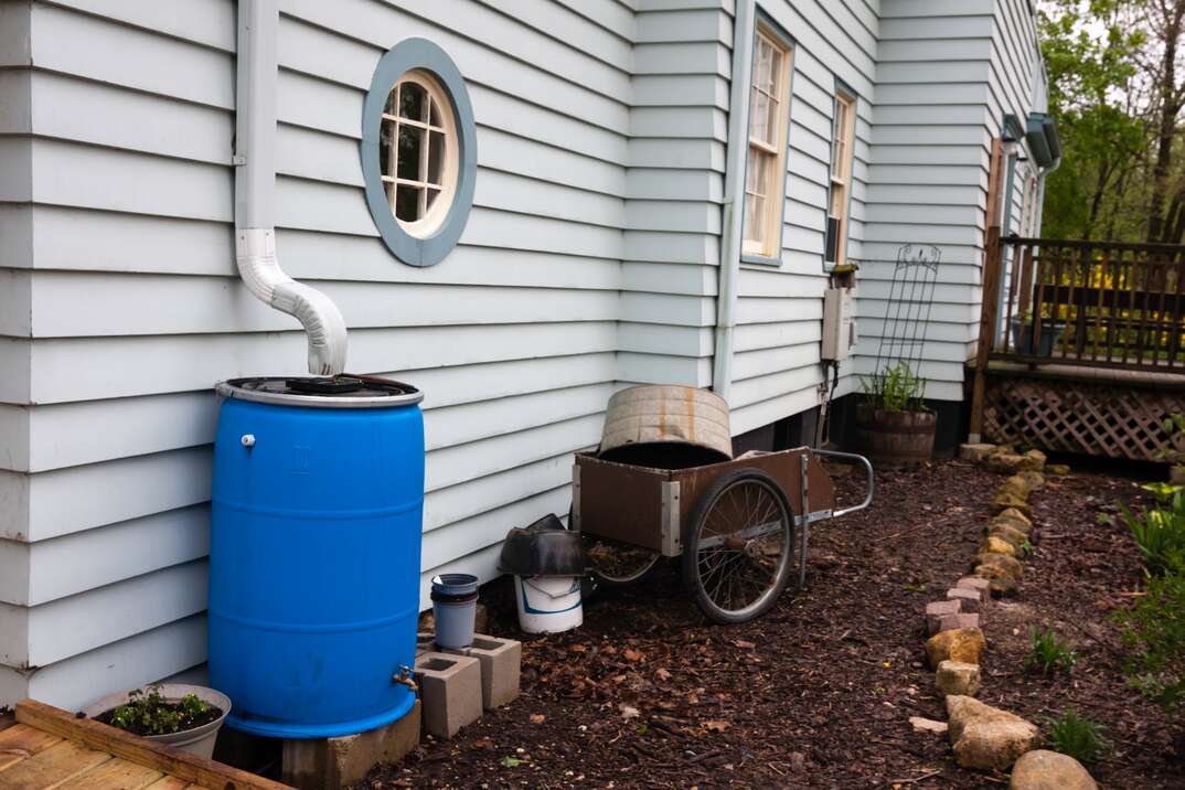 a blue Rain Barrel rests under a white gutter on a home to collect rainwater