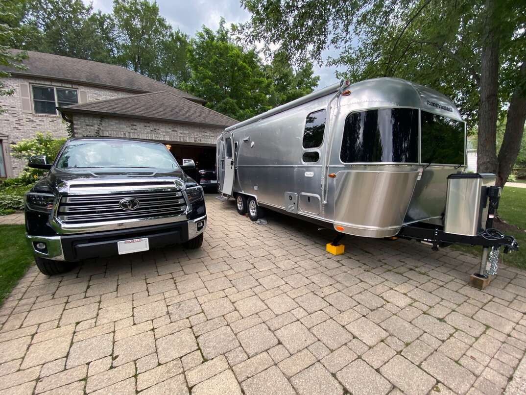 photo of a crowded residential driveway with both a toyota tundra and airstream travel trailer parked side by side 