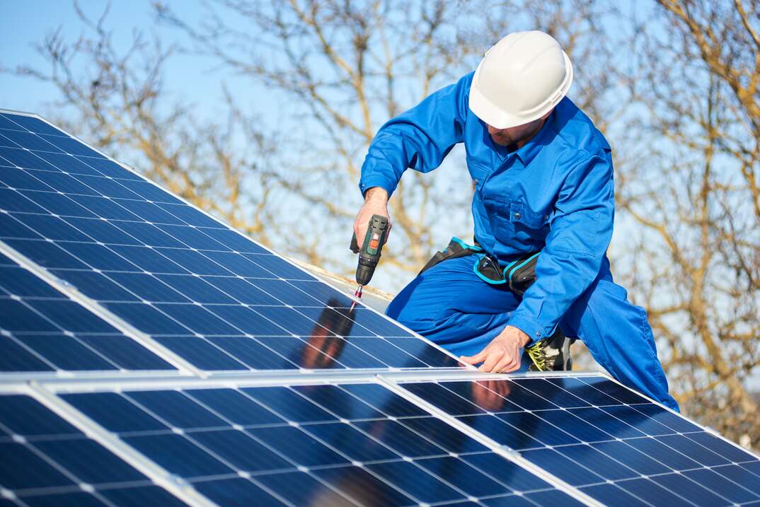 Electrician mounting solar panel on roof of modern house