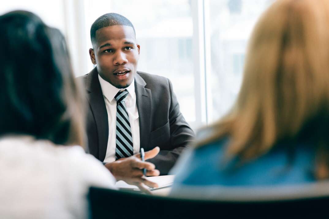 A male professional in a business suit faces two women with their backs to the viewer and explains something to them, male professional in a suit, male professional, professional, male, two women, women, clients, lawyer, financial planner, business office, lawyer's office, law office, financial office, accountant, accountant's office