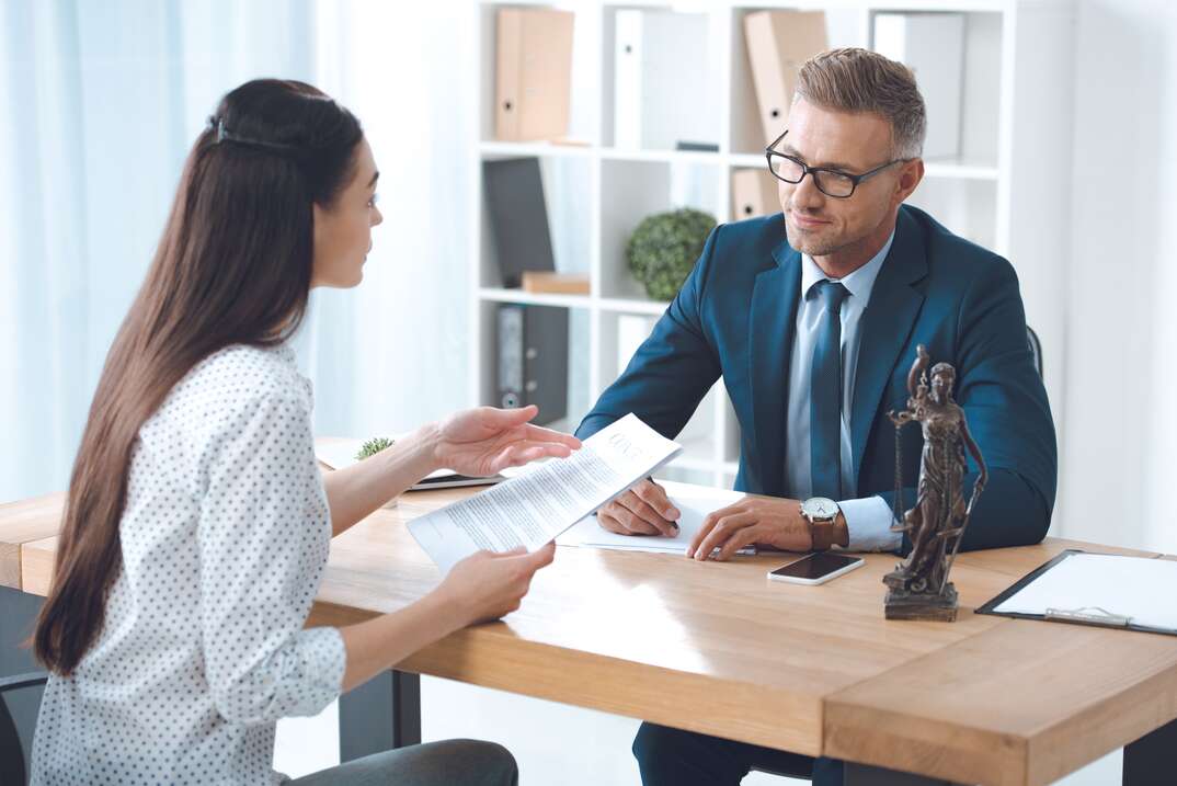 lawyer and client looking at each other while discussing papers in office