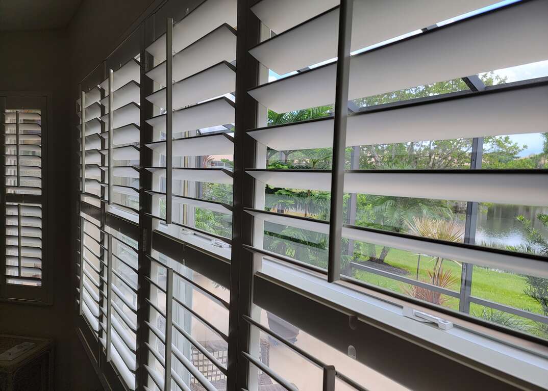 Plantation shutters in a window looking out to a screened in patio with natural light coming through