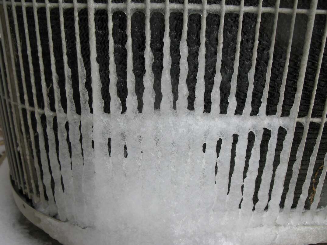 A closeup of an outdoor air conditioning unit that has frozen over
